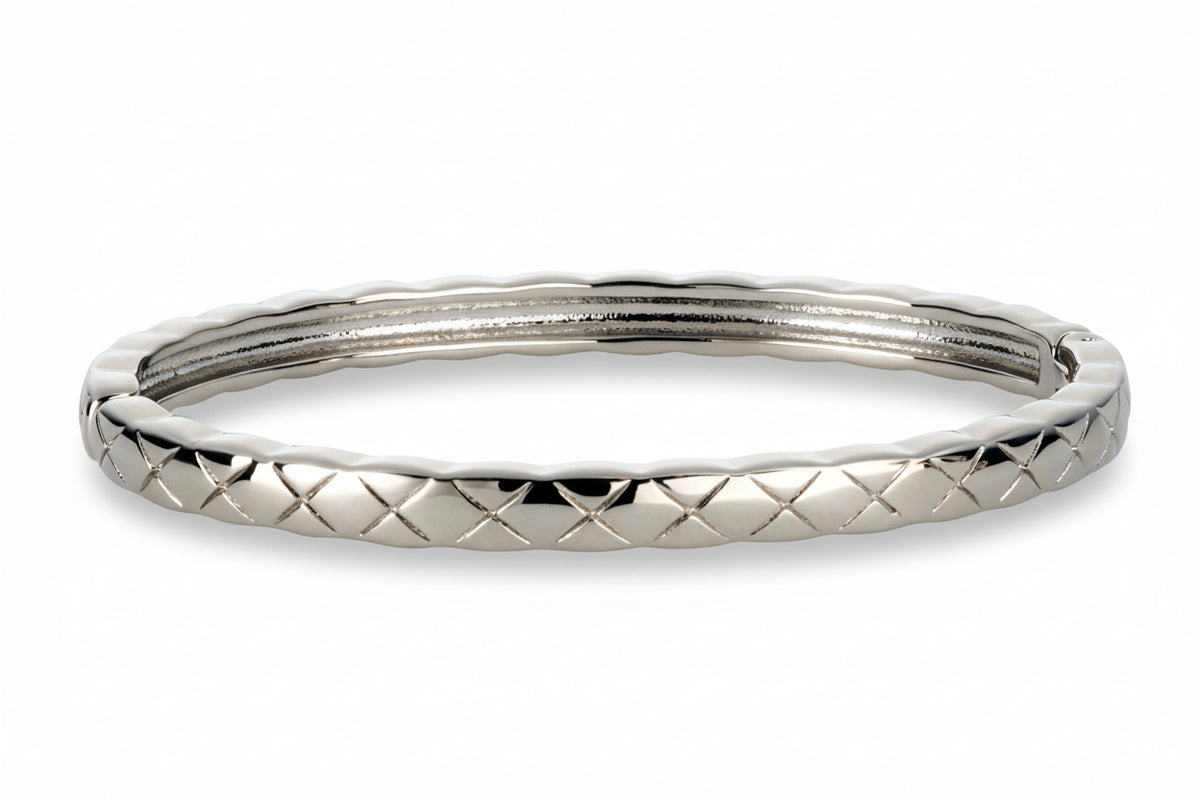 Silver-tone stainless steel bangle bracelet featuring an engraved crisscross quilted pattern and polished finish.