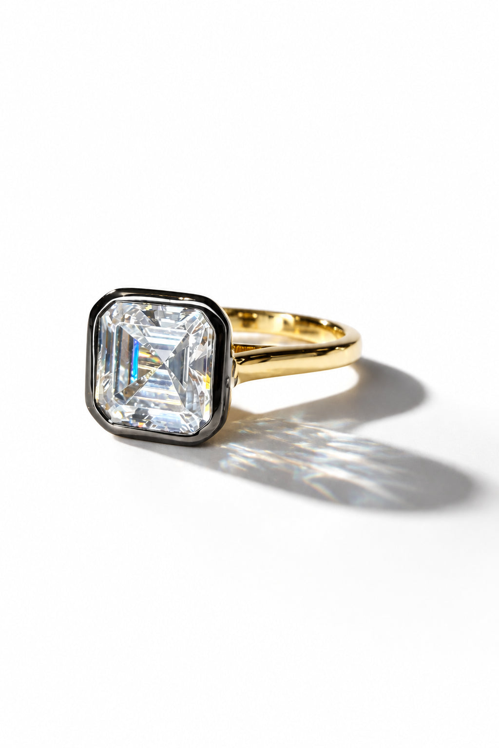 A yellow gold ring featuring a large, square step-cut clear cubic zirconia gemstone in a bezel setting with a black border, shown on a plain white background.
